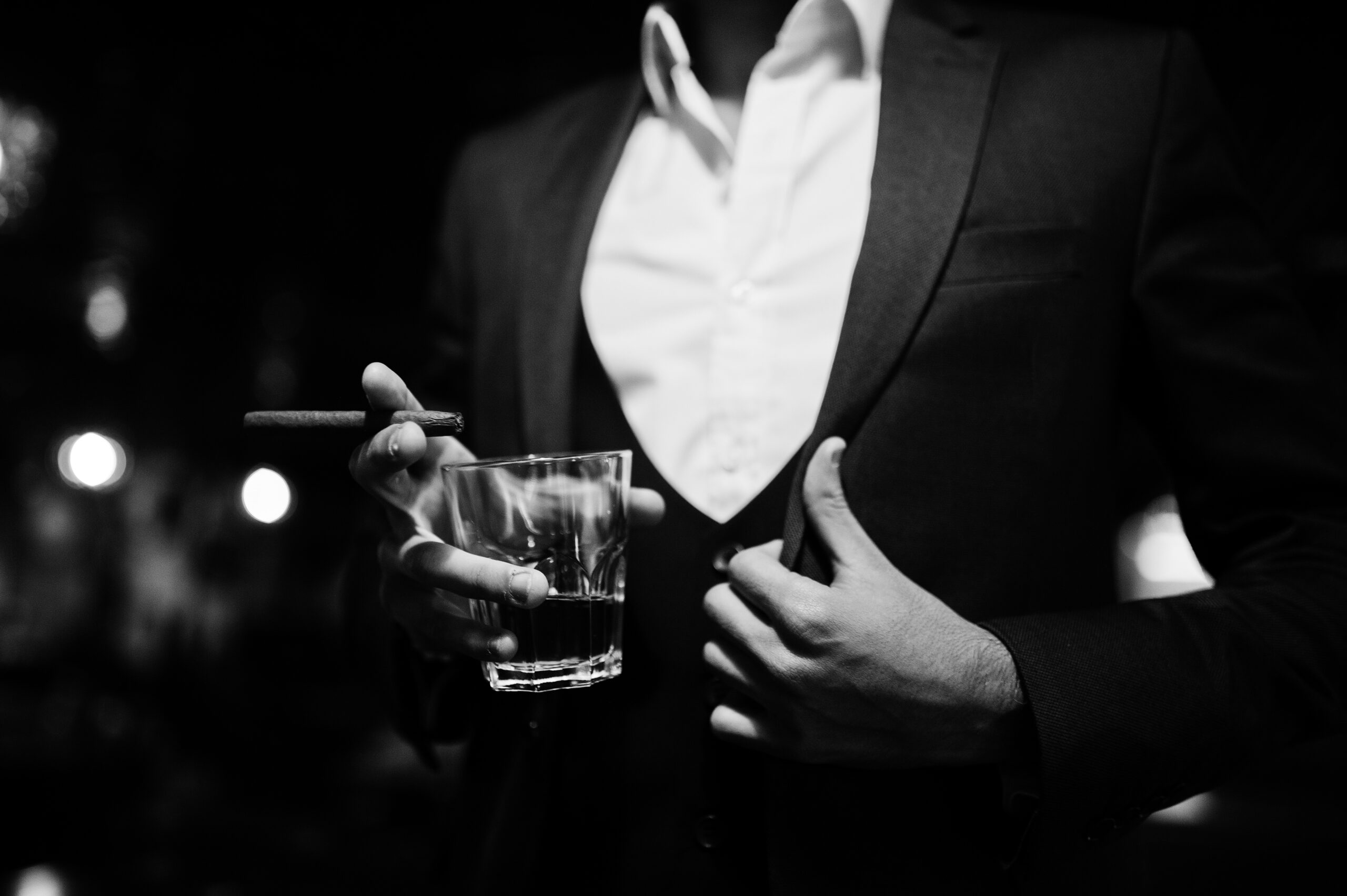 groom in a three piece suit holding a glass of whiskey and a cigar